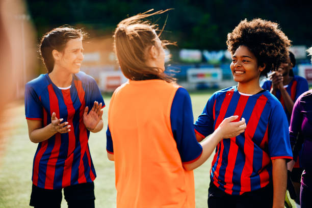 Happy black player and her teammates after soccer match on playing field. Happy African American soccer player talking to her teammates after successful game on playing field. club soccer photos stock pictures, royalty-free photos & images