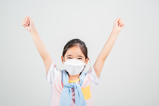 Asian little child girl wearing respirator mask to protect coronavirus outbreak and pointing hand to blank background, New virus Covid-19