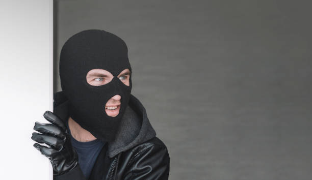 istock An evil thief in mask looks out from behind a white board. Space for text and design. copy space. the surprised bandit looks away 1485991589