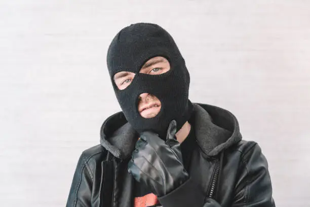 Photo of thief in a black jacket. A man in a black balaclava with an evil expression on his face. An aggressive bandit on a white background. The concept of crime or theft.