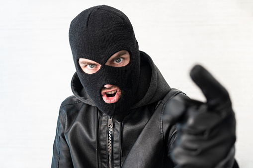 A thief in a black jacket. A man in a black balaclava with an evil expression on his face. An aggressive bandit on a white background. The concept of crime or theft.