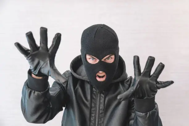 Photo of thief in a black jacket. A man in a black balaclava with an evil expression on his face. An aggressive bandit on a white background. The concept of crime or theft.