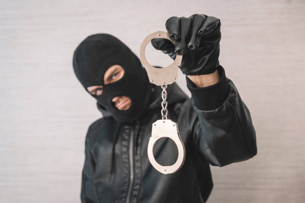 bandit in a black mask and gloves with handcuffs in his hands on a white background. Release from imprisonment. Prison break concept. a bandit in a black mask and gloves with handcuffs in his hands on a white background. Release from imprisonment. Prison break concept. Jailbreak wrongdoer stock pictures, royalty-free photos & images