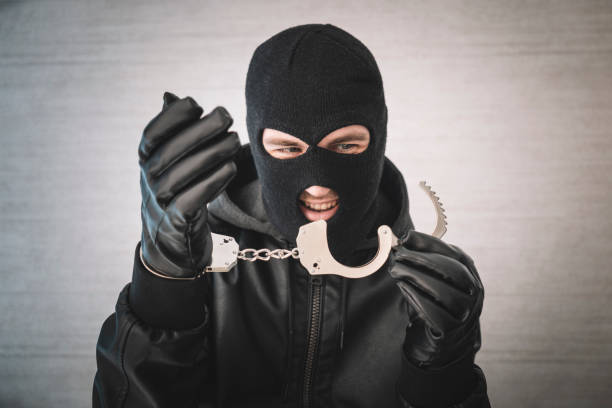 bandit in a black mask and gloves with handcuffs in his hands on a white background. Release from imprisonment. Prison break concept. Jailbreak a bandit in a black mask and gloves with handcuffs in his hands on a white background. Release from imprisonment. Prison break concept. Jailbreak wrongdoer stock pictures, royalty-free photos & images