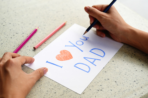 Hand drawing text 'I Love You Dad' on a card,  preparing a greeting card for Father's Day.