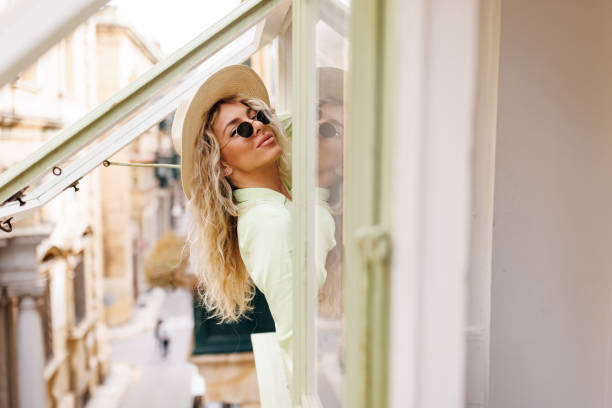 Beautiful young woman looking through window, view from outside