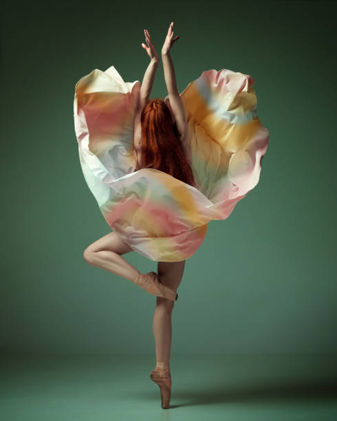 istock Young classical dancer wearing colorful flying dress dancing on fingertips over dark green studio background. Tender movement 1485995959