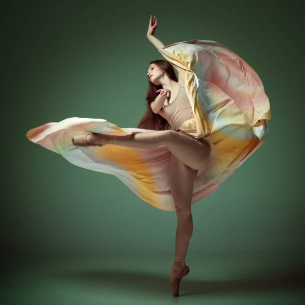 istock Young classical dancer wearing colorful flying dress dancing on fingertips over dark green background. Tender soul 1485996026