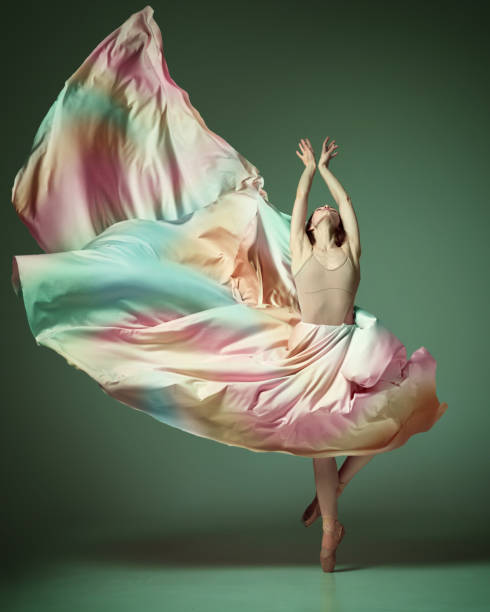 istock Charming ballerina dancing elegant, grace movement with flying fabric over dark green studio background. Rainbow dress 1485996121
