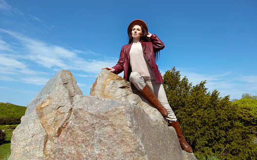 A young adult woman sits on a stone and enjoys her day surrounded by plants against the backdrop of an endless blue sky. Her long hair is flowing freely as she rests. American woman bottom view