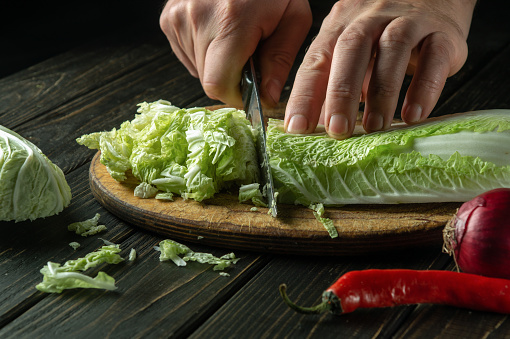 Close-up of a cook hands cut green leaves lettuce on a cutting board with a knife for preparing vegetarian food. Delicious breakfast concept on dark background