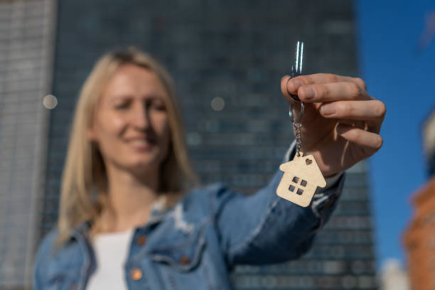 Woman holding house keys outdoors, closeup with space for text. Real estate agent Close-up focus on keys with cute keychain in shape of house in women's hands,homeowner celebrates moving new apartment mujer sosteniendo las llaves de la casa al aire libre, primer plano con espacio para el texto. agente inmobiliario enfoque de cerca en llaves con lindo llavero en forma de casa en manos de mujeres, propietario celebra mudarse nuevo apartamento