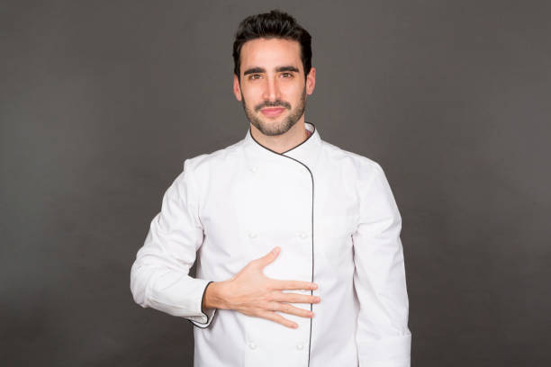 Young male cook touching belly, looking at camera