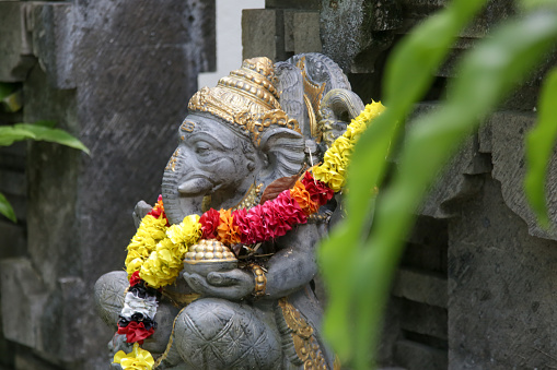 Traditional Ganesha statue with flower wreath in Balinese garden. Lord Ganesha is believed to bring good luck and thus he is worshipped before anything new is started.