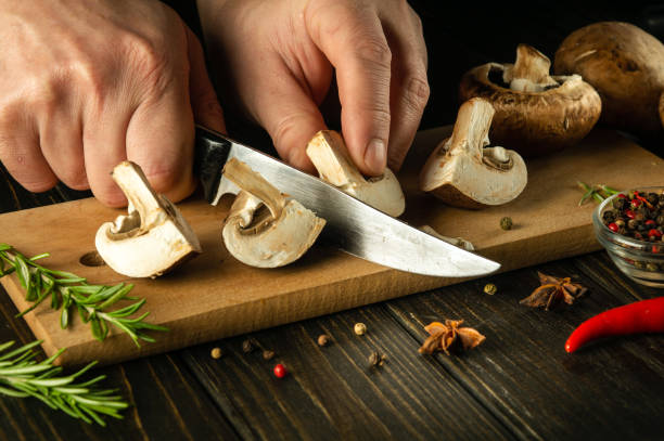 istock Close-up of a cook hands with a knife cutting mushrooms on a cutting kitchen board while preparing a vegetarian breakfast. Delicious mushroom diet with spices. 1486004516