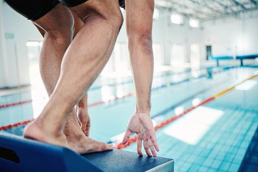 Sports, swimming and man on diving board by pool for training, exercise and workout in competition. Fitness, motivation and professional male athlete ready to dive, start and triathlon race on podium