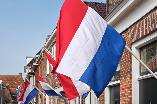 Dutch flags waving in the wind in a typical dutch street on Koningsdag in the Netherlands. King's day is a national holiday in the Kingdom of the Netherlands