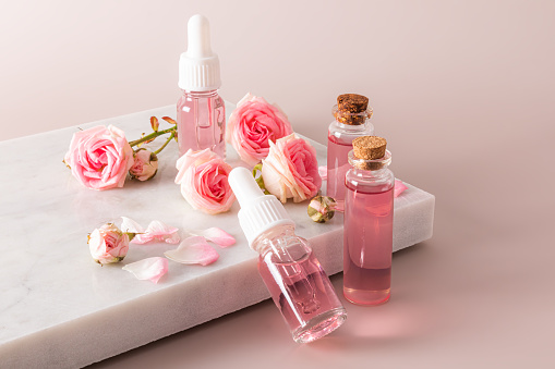 cosmetics in various bottles with a white cap and pipette, a prbka on a white marble podium and a pink background. Gentle light self-care