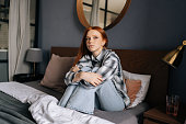 Portrait of sad young woman sitting alone on bed hugging knees in bedroom, crying looking away. Desperate pretty female feeling disappointment about something