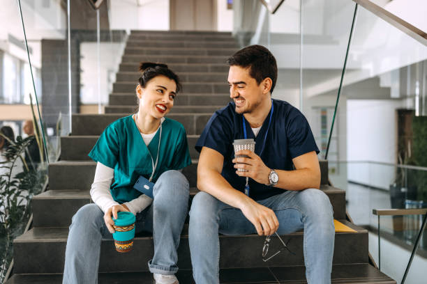 Healthcare workers casually talking while having coffee break at hospital, sitting on the stairs