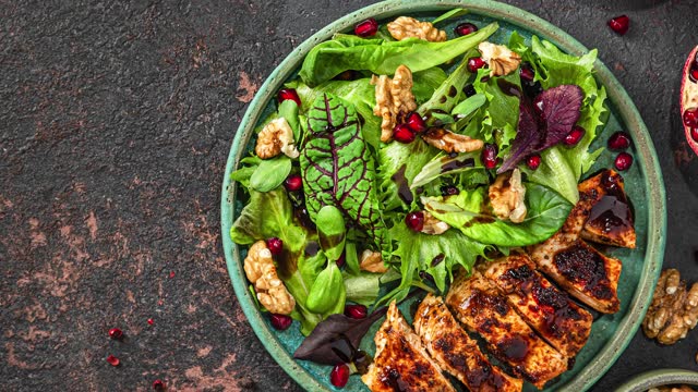 Salad with grilled chicken fillet, mix greens, walnuts, pomegranate and balsamic sauce on black background