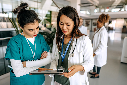 Two female doctors using digital tablet and talking in modern hospital corridor