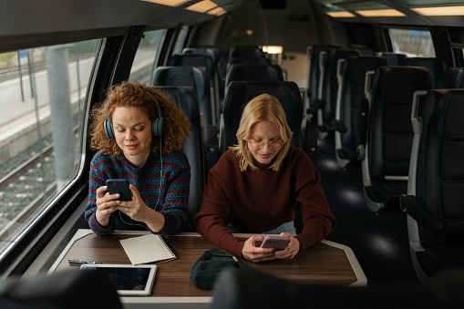 Young smiling women using their smart phone while going on a trip by train.