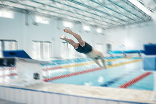 istock Swimming, action and man diving in pool for training, exercise and workout for competition at gym. Fitness, sports and motion blur of professional male athlete for dive, jumping and triathlon race 1486027341
