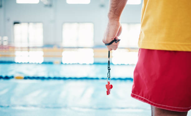 Hands, lifeguard and whistle by swimming pool for water safety, security or ready for rescue indoors. Hand of expert swimmer holding signal tool for warning, safe swim or responsibility for awareness Hands, lifeguard and whistle by swimming pool for water safety, security or ready for rescue indoors. Hand of expert swimmer holding signal tool for warning, safe swim or responsibility for awareness lifeguard stock pictures, royalty-free photos & images