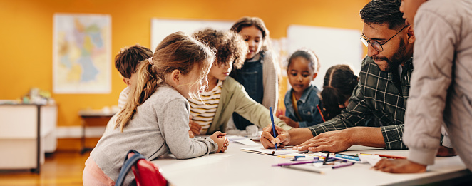 Art and creativity in an elementary school class. Teacher shows his students how to draw using a colouring pencil in a classroom. Primary education and child mentorship.