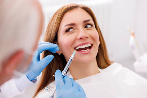 Dentist applying local anesthetic to female patient stock photo