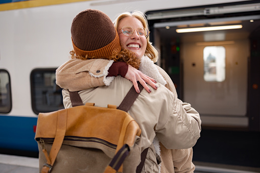 Happy woman embracing her friend after arriving by train at the station.