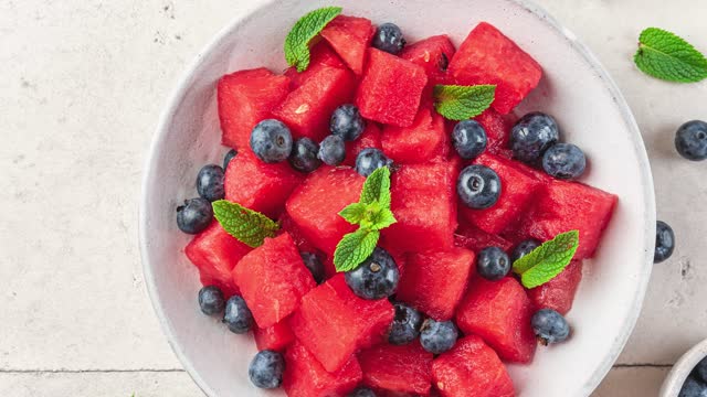 Fruit salad with watermelon, blueberry, lime juice and mint in a plate on white table. top view with copy space