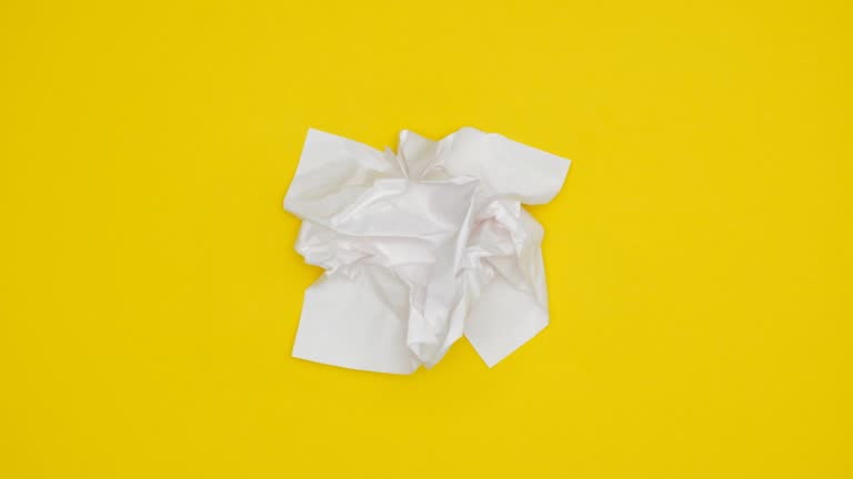 Blank sheet of white paper appears on yellow background  from a paper ball, wrinkles again and disappears. Looping stop motion animation. 4K video.