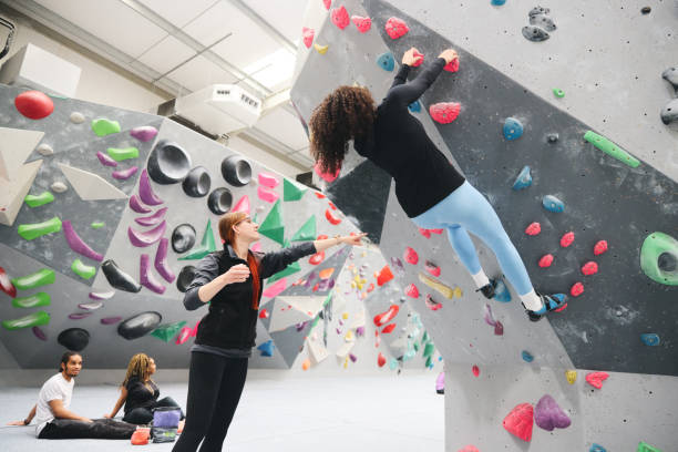 istock Multi-Cultural Group Watching Friend On Climbing Wall In Indoor Activity Centre With Coach 1486032147