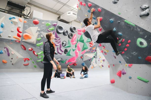 istock Multi-Cultural Group Watching Friend On Climbing Wall In Indoor Activity Centre With Coach 1486032164
