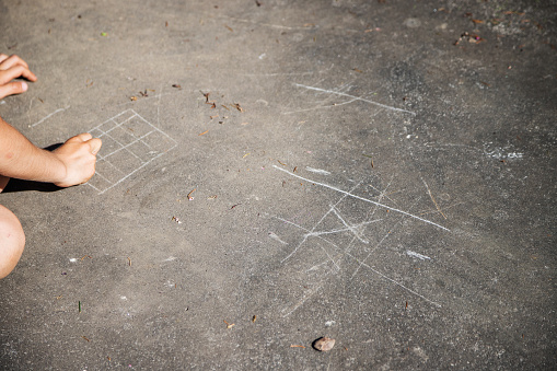Happy childhood. Caucasian children playing outside during the day, scratching the ground with a rock to play the classic game of tic-tac-toe. Copy space