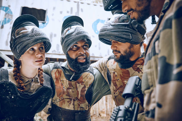 istock Paintball, team or friends together for a game while planning and talking strategy for attack or action. Diversity men and women group for military, soldier or army person in outdoor battlefield 1486039312