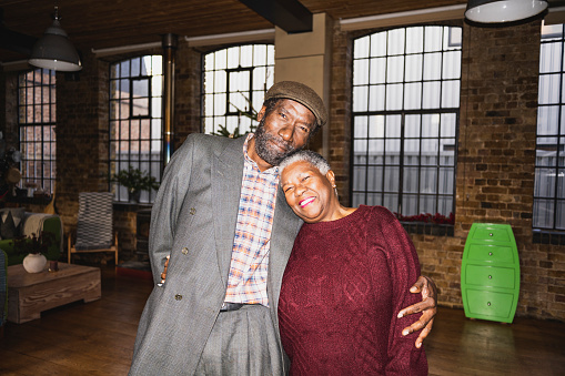 Waist-up view of man and woman standing with arms around each other, heads together, and smiling at camera. On-camera flash, retro-style photographic effect.