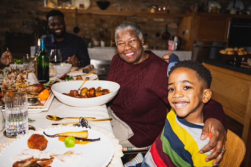 Multi-generation Black family, focus on senior woman with arm around grandson, both grinning at camera. On-camera flash, retro-style photographic effect.