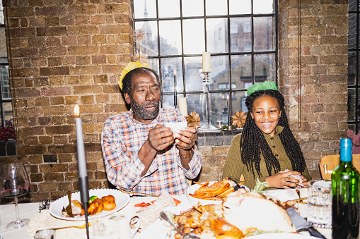 Waist-up view of 12 year old girl listening to her grandfather and laughing as they enjoy a British tradition. On-camera flash, retro-style photographic effect.