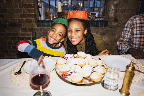 ミンスパイとクリスマスクラッカーの帽子をかぶった子供たち - dining table flash ストックフォトと画像