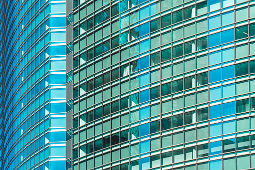 close up of a modern corporate building with angular patterned mirrored windows panes reflecting the sky and clouds