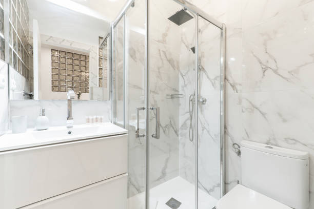 istock Bathroom with porcelain sink, shower tray, rectangular frameless mirror and walls covered in white marble with gray veins 1486050059