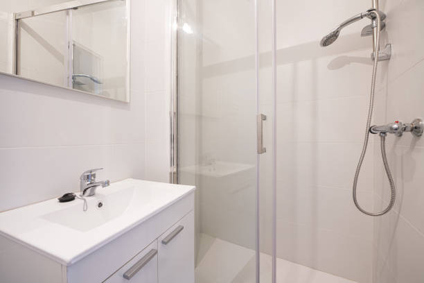 istock Small bathroom with white lacquered wood cabinets with doors, frameless mirror on the wall, stainless steel fixtures, porcelain sink, and walk-in shower with glass partitions 1486050142
