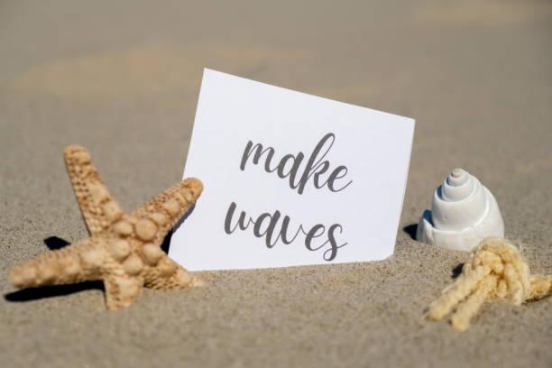 istock MAKE WAVES text on paper greeting card on background of starfish seashell summer vacation decor. Sandy beach sun coast. Holiday concept postcard. Getting away Travel 1486050346