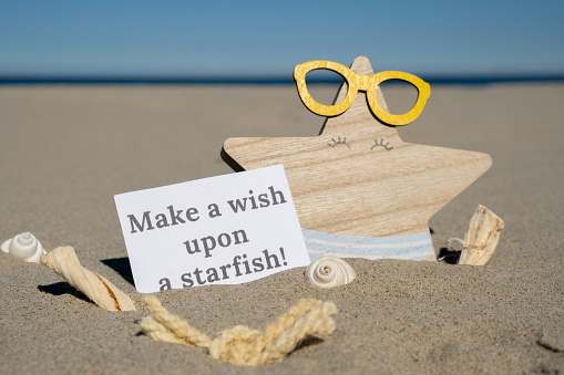 MAKE A WISH UPON A STARFISH text on paper greeting card on background of funny starfish in glasses summer vacation decor. Sandy beach sun coast. Holiday concept postcard. Getting away Travel Business concept