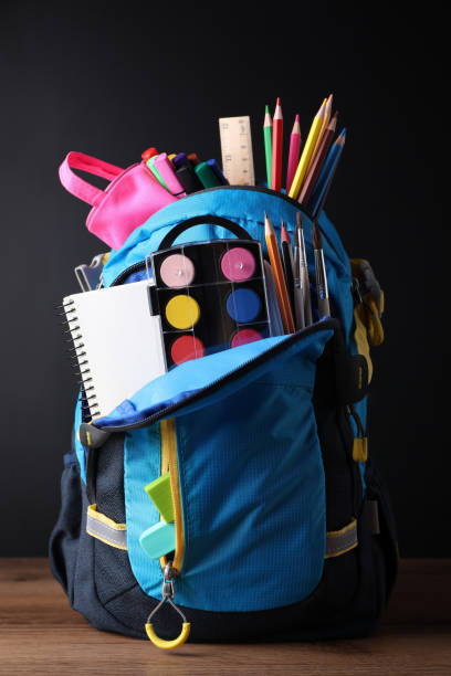 istock Backpack with different school stationery on wooden table near blackboard 1486051551