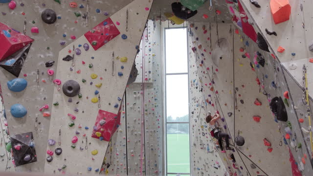 A Caucasian Sportswoman High Up On A Climbing Wall In An Indoor Climbing Center