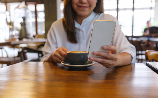 istock Closeup image of a young woman holding and using mobile phone while drinking coffee in cafe 1486058649